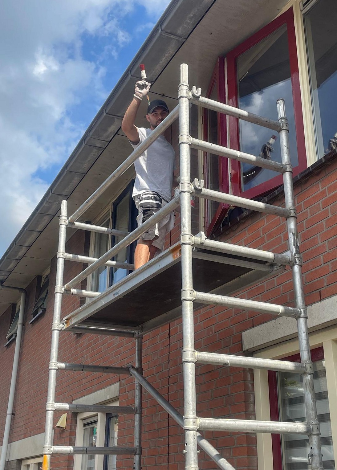 Schilder op een rolsteiger aan rode kozijnen