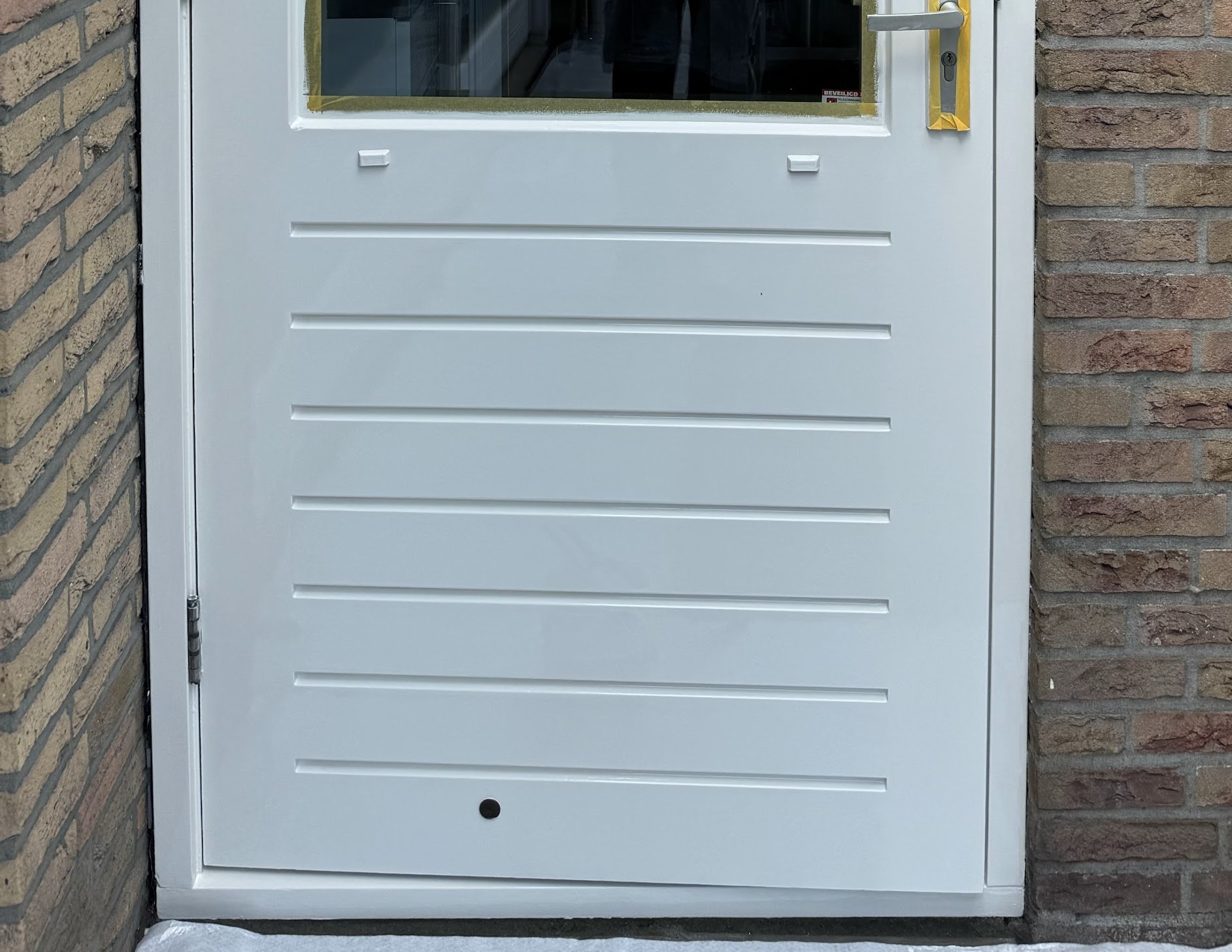Wit geschilderde deur met liggende panelen tussen het metselwerk